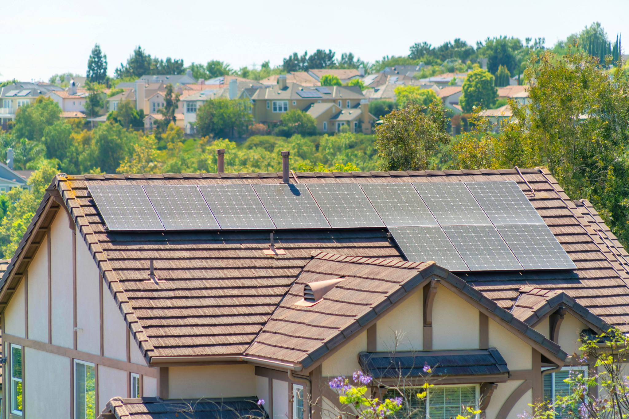 Brown tile roof with solar panels on it surrounded by lush green trees in a rural town